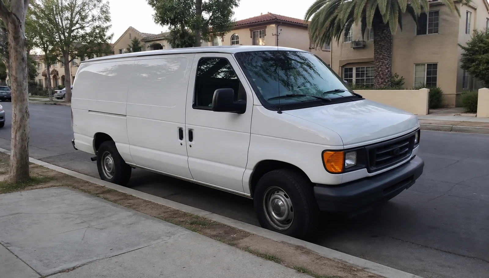 A plain white work van parked on a quiet residential street